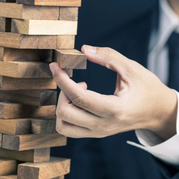 man in business suit pulls a piece out of wobbly wooden tower
