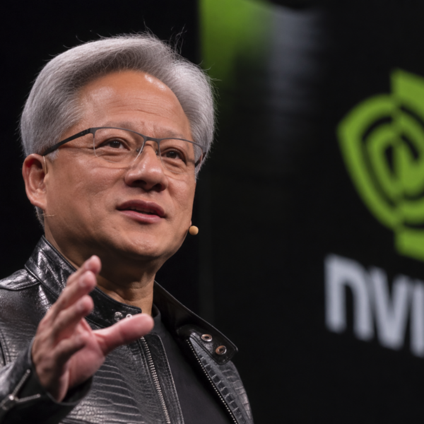 Jensen Huang speaks on stage beside a large Nvidia logo during a technology event.