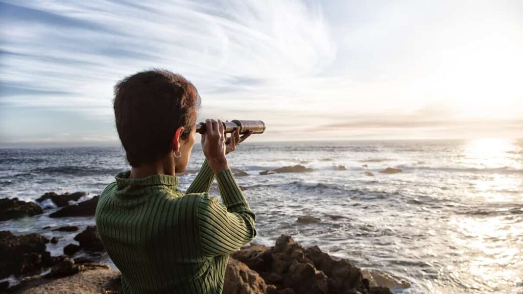 person with spyglass looks at ocean horizon